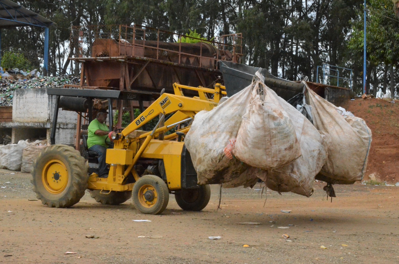 Trator transportando grandes sacos de material reciclável em um pátio de triagem
